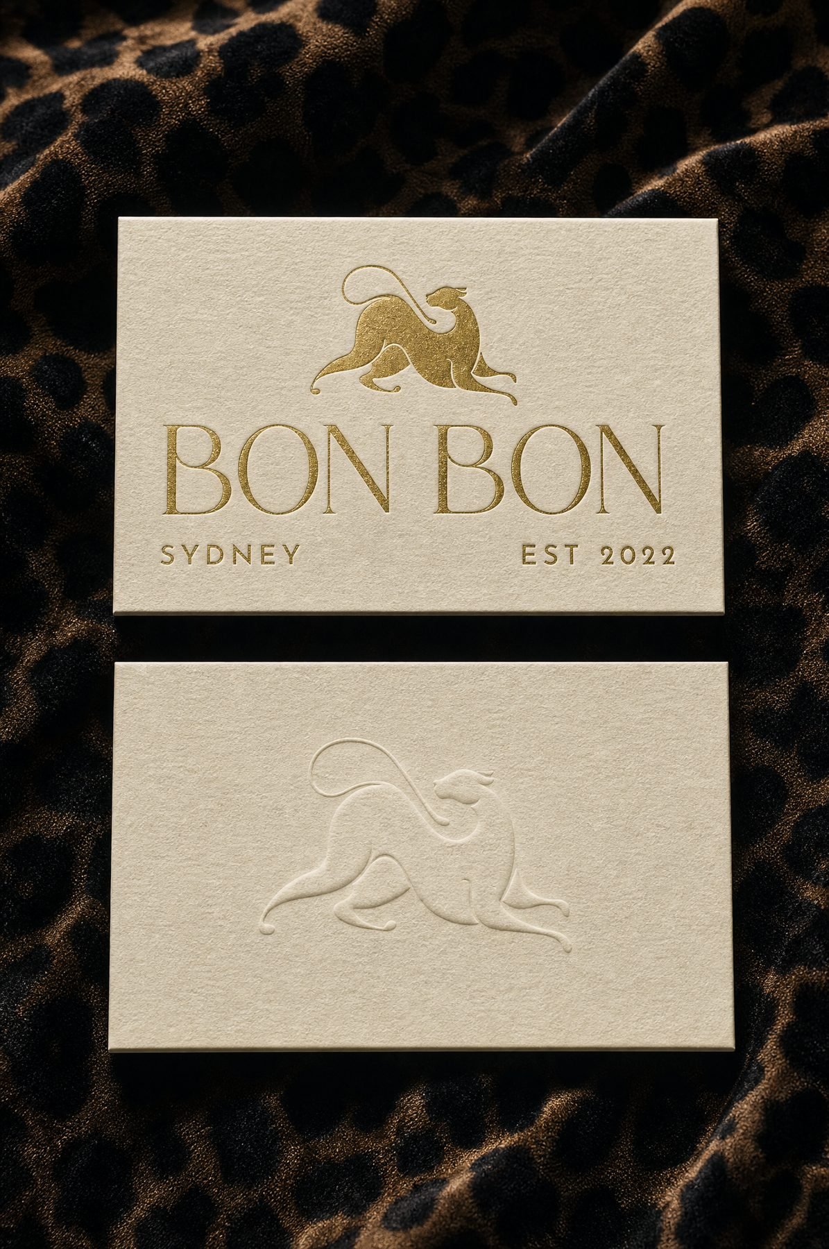 Ivory business cards with the centred logo in gold foil and a blind-debossed leopard.